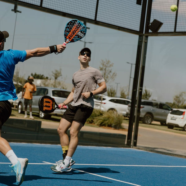 Two men playing padel tennis on outdoor blue court