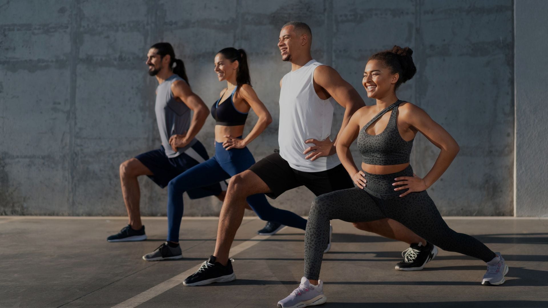 Group of people in athletic wear posing in front of a concrete wall.
